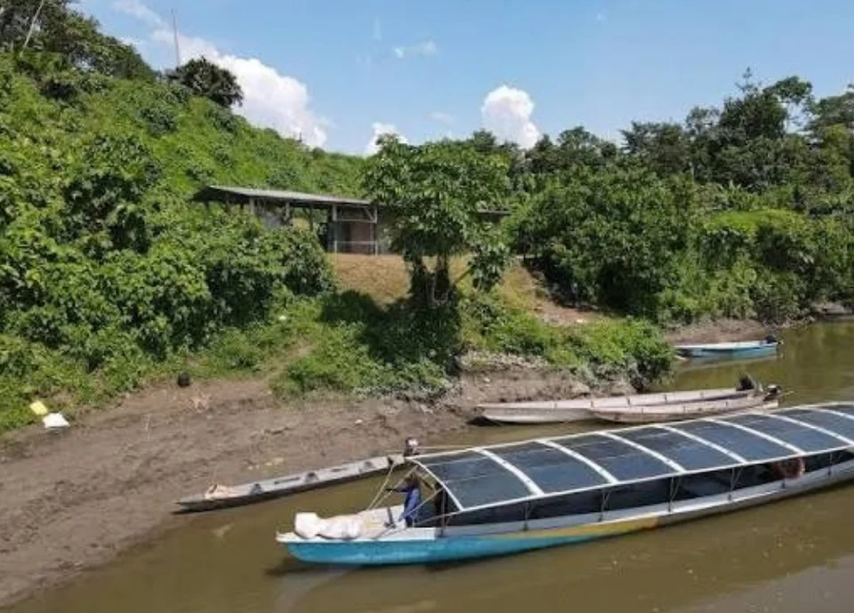 A solar-powered river boat moored at a muddy bank of an Amazon river.